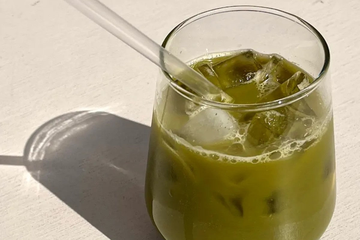 Iced green matcha drink in a glass with a clear straw on a white surface, representing nutritional support for the gut-brain connection and digestive wellness
