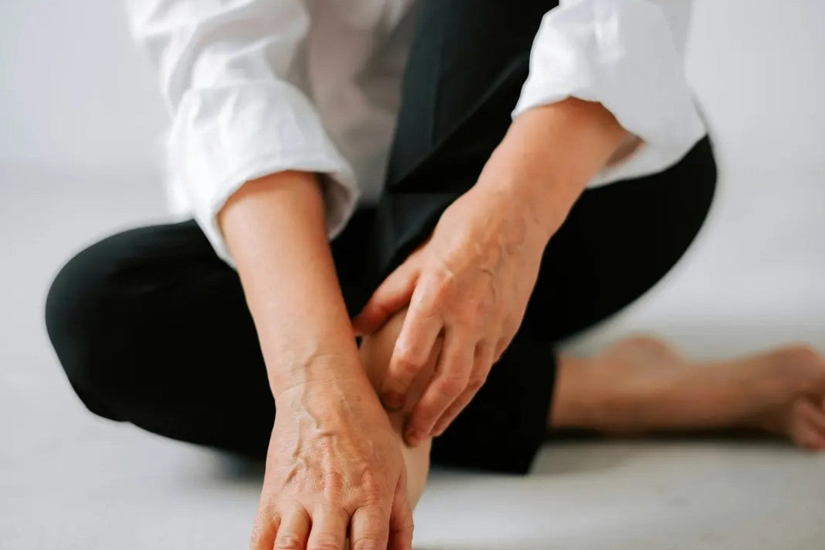 Woman in a white blouse with hands clasped over crossed legs, representing the discomfort of hot flashes and menopause symptoms