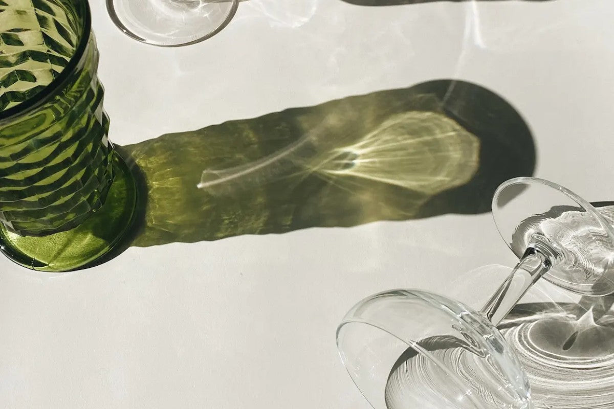 Green glass tumbler and wine glass with dramatic light shadows, representing a THC vs. alcohol wellness comparison