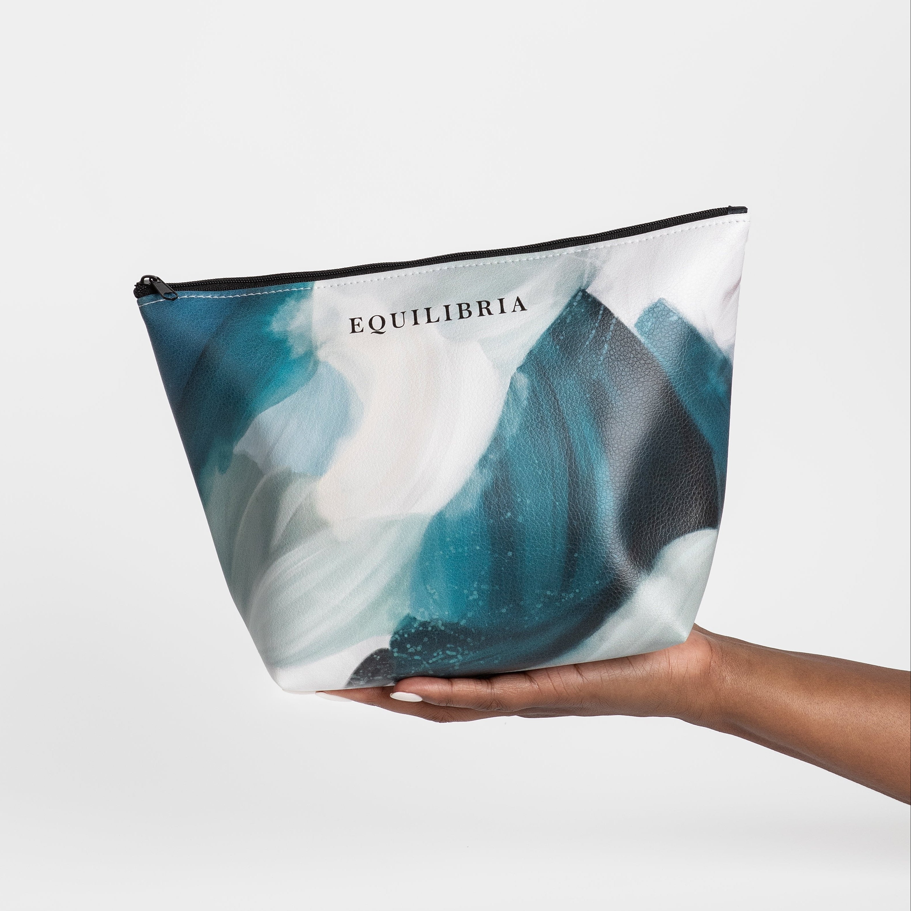 A person holding a large blue and white cosmetic pouch with the brand name 'EQUILIBRIA' printed on it.