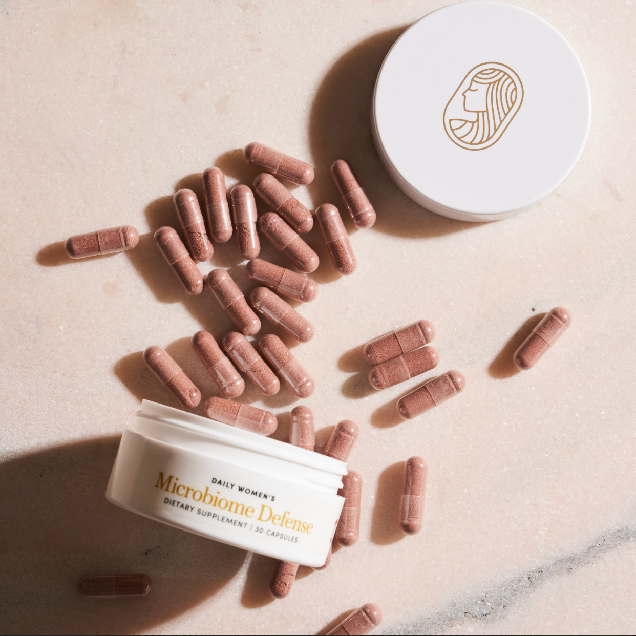 Women's microbiome capsules and containers on a marble surface