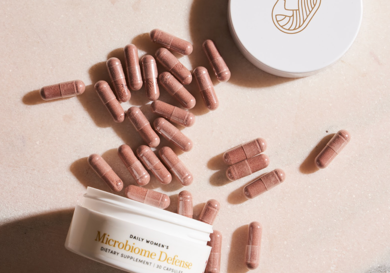Women's microbiome capsules and containers on a marble surface