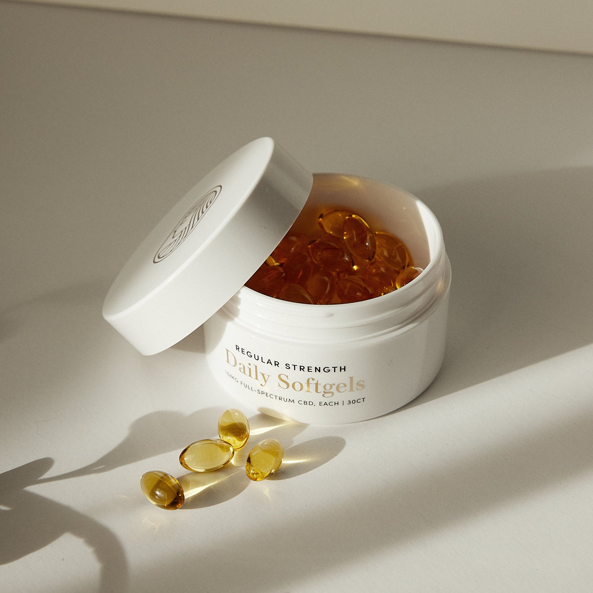 Jar of daily high quality CBD softgels with open lid on a light background