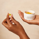 Person holding a jar of Daily Softgels and a softgel capsule against a beige background