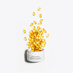 Yellow softgels spilling out of a white container labeled 'Daily Softgels' on a white background