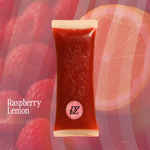 Packaged raspberry lemon fruit freeze pop with raspberries and a sliced orange in the background