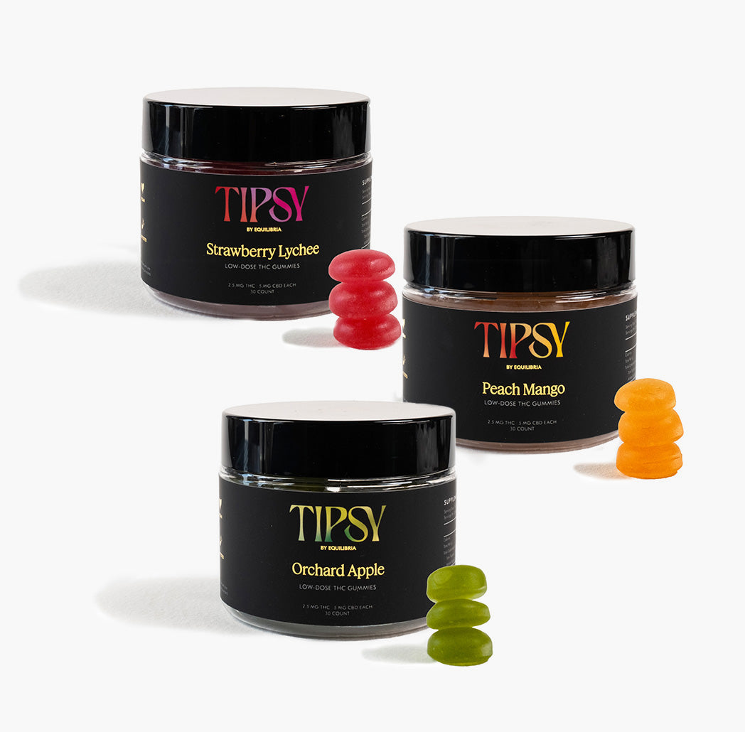 Three containers of Tipsy THC Gummies in different flavors: Strawberry Lychee, Peach Mango, and Orchard Apple, with gummy candies in those respective flavors displayed in front of each container.